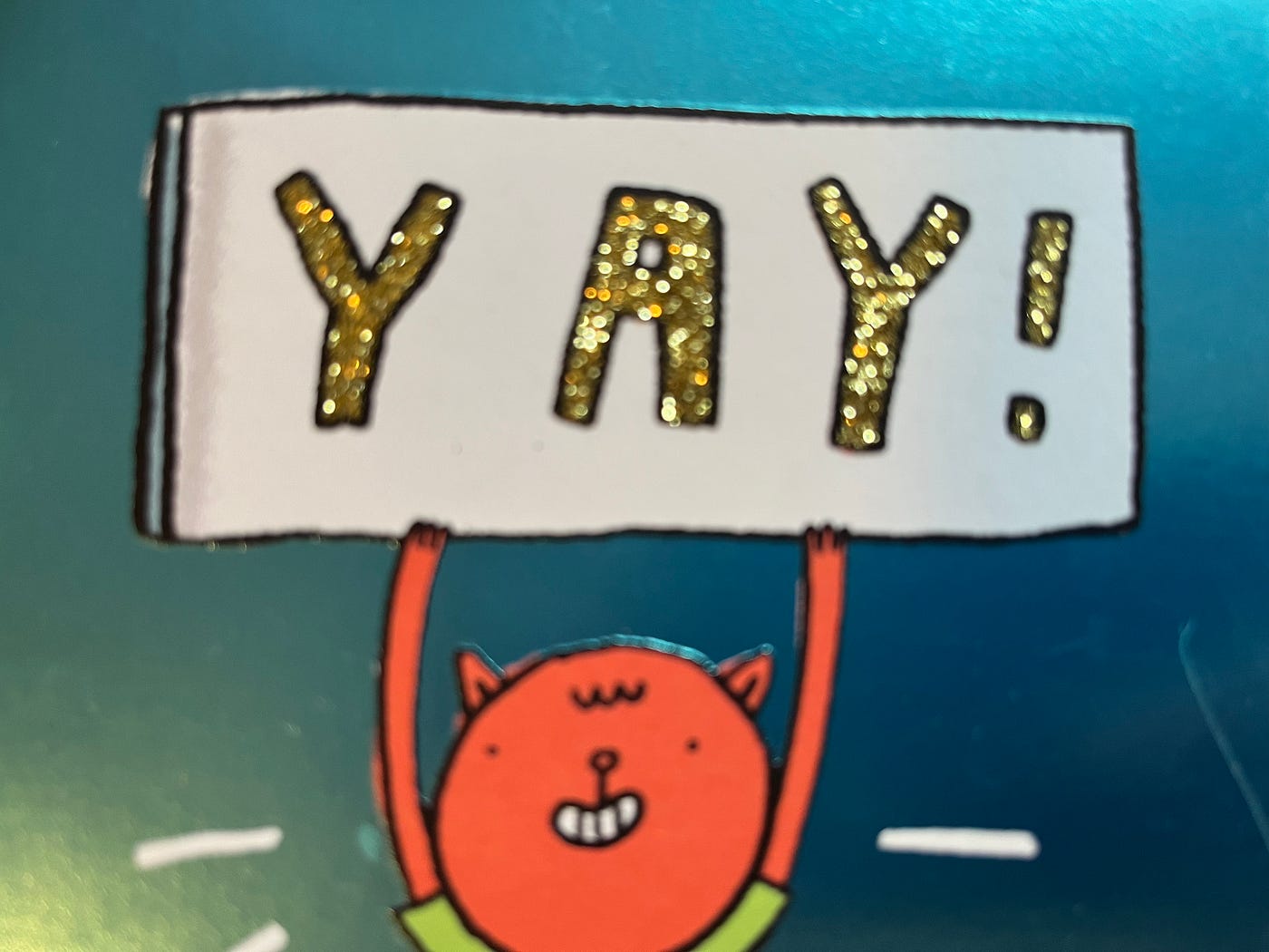A cartoon creature holds up a sign that says "YAY!" in sparkly letters.