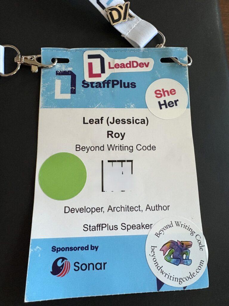 A StaffPlus badge for Leaf (Jessica) Roy, Beyond Writing Code. Developer, Architect, Author. StaffPlus Speaker. The badge is decorated with a green dot sticker, a pin that says DX, and stickers that say LeadDev, She/Her, and Beyond Writing Code beyondwritingcode.com. 