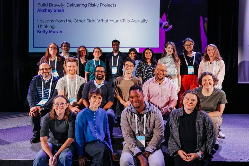 A group photo of about 20 people standing, kneeling, or sitting on a stage. I'm in a green shirt, kneeling, on the right.