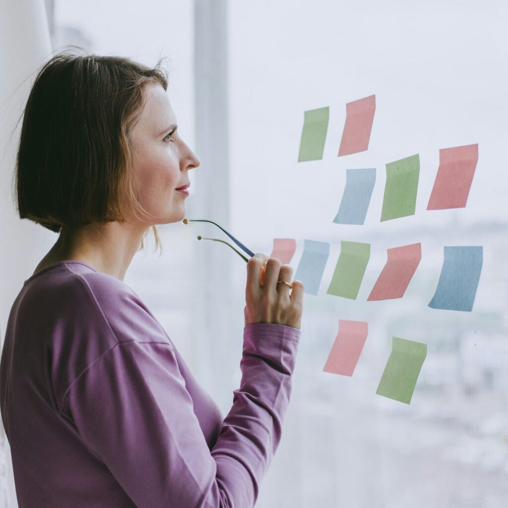 A person holding their glasses stands facing a window with several blank sticky notes